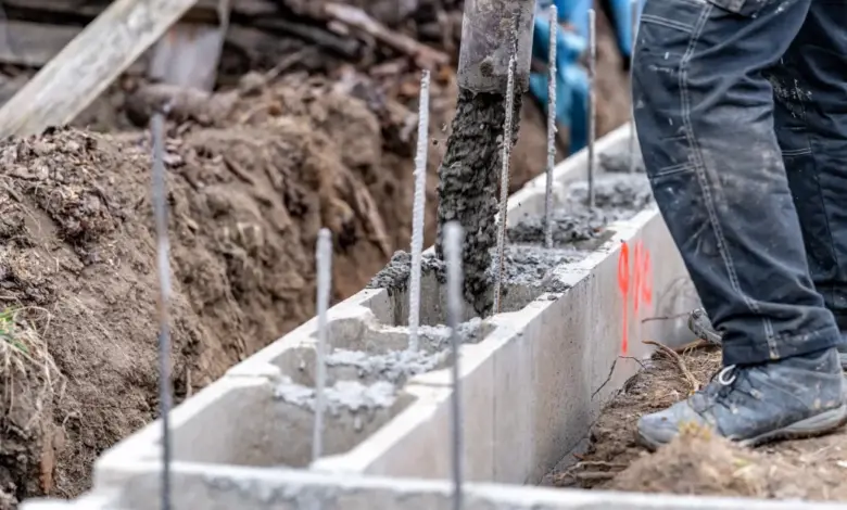 Stavebník nalévá beton do příkopu pro plot.