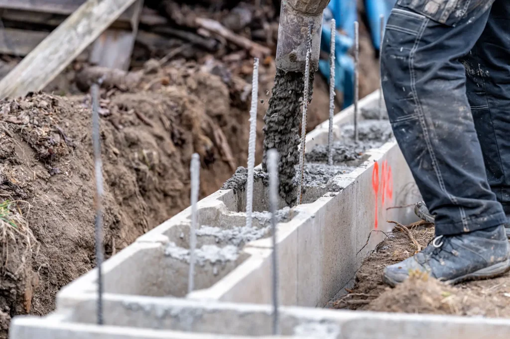 Stavebník nalévá beton do příkopu pro plot.