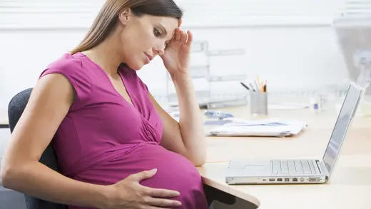 Těhotná žena sedí u počítače s bolestmi břicha.