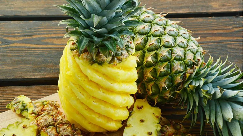 Celý ananas vedle oloupaného s vybraným jádrem na dřevě.
