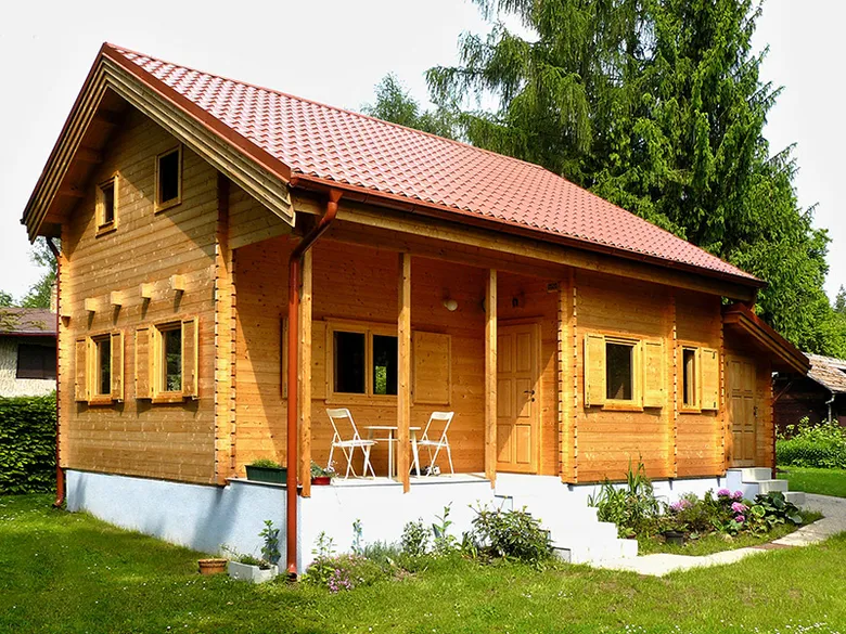 Dřevěná chata s červenou střechou na trávníku.