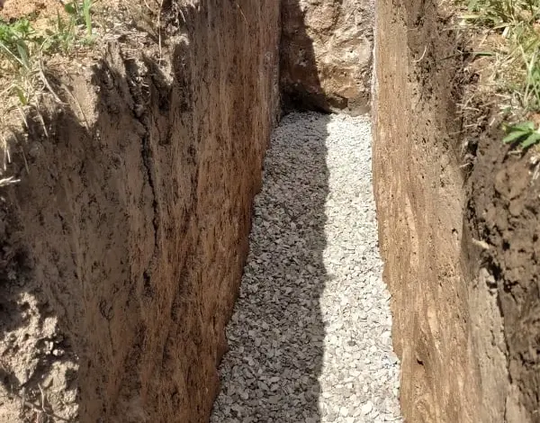 Zásyp štěrkem pro drenáž kolem domu – výkop s vrstvou kameniva.