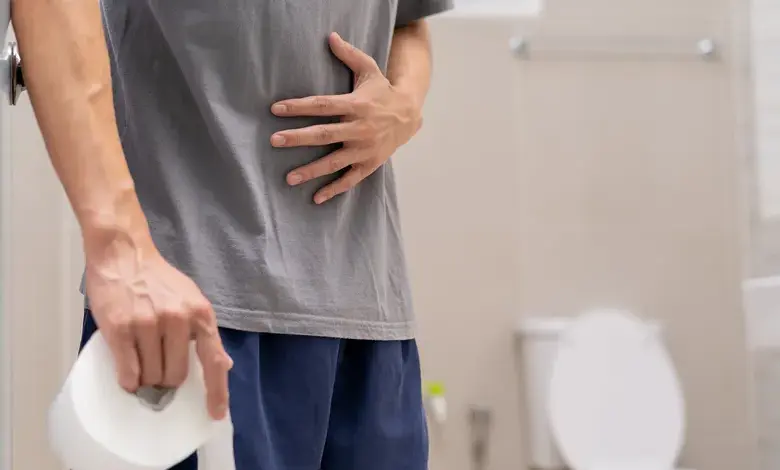 Muž drží toaletní papír v koupelně s bolestí břicha.
