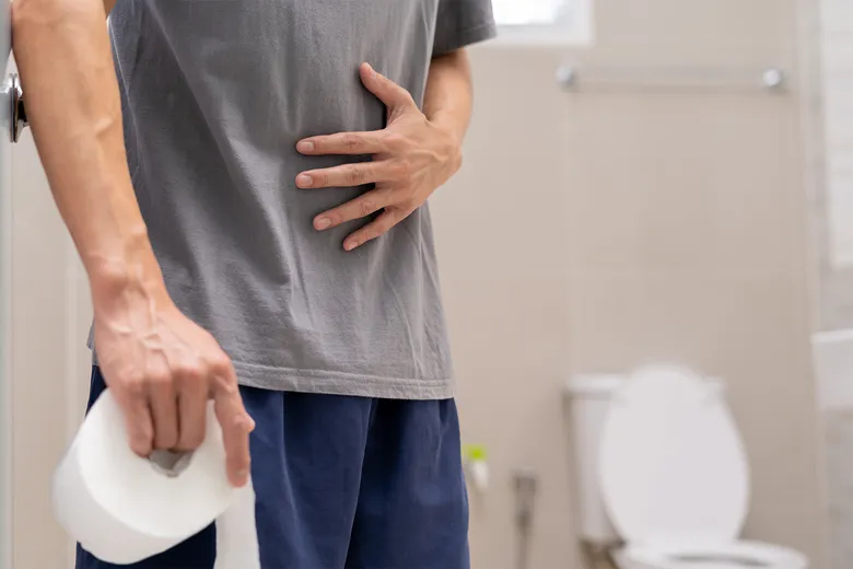 Muž drží toaletní papír v koupelně s bolestí břicha.