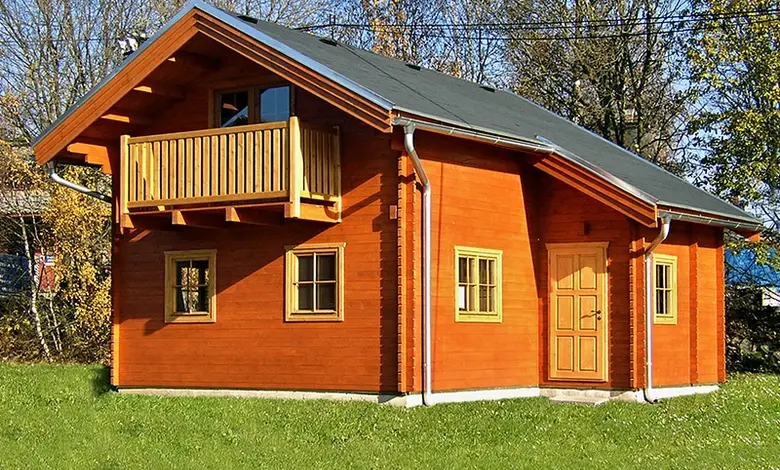 Dřevěná chata na trávníku s balkónem a okny.