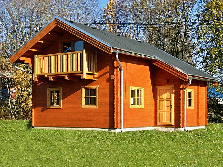 Dřevěná chata na trávníku s balkónem a okny.