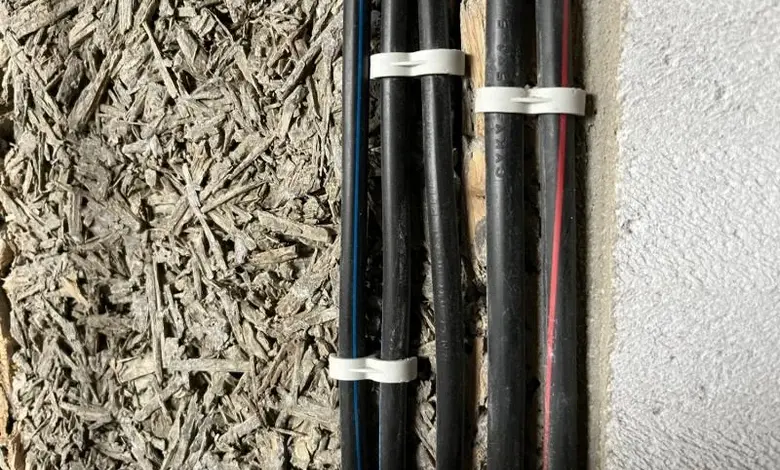 Černé elektrické kabely v zdivu s izolačním materiálem.