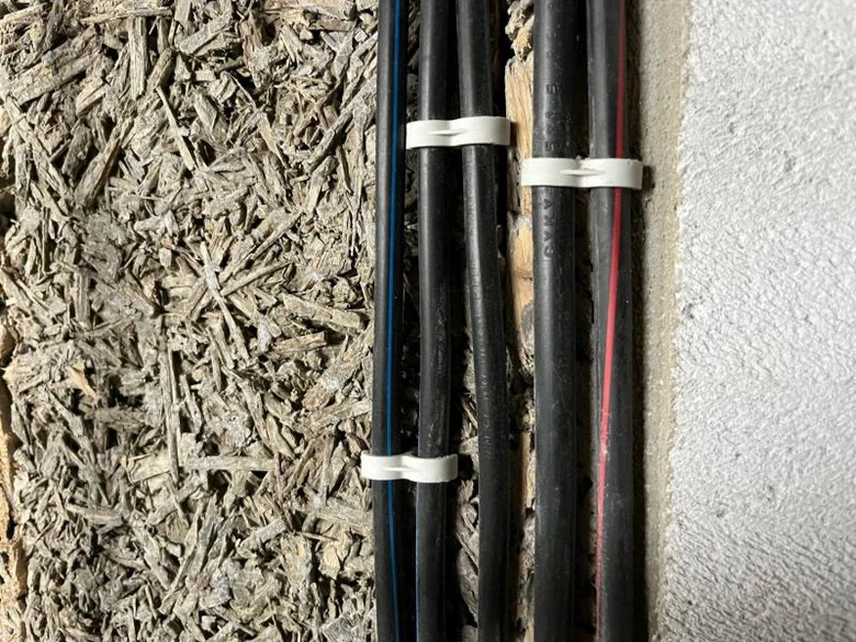 Černé elektrické kabely v zdivu s izolačním materiálem.