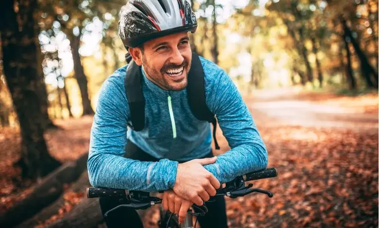 Usměvavý cyklista v lese s podzimními listy.