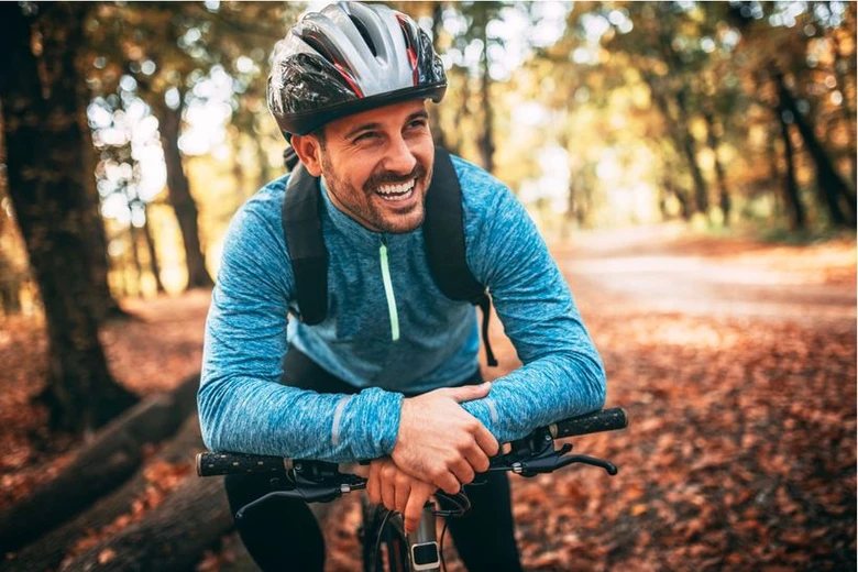 Usměvavý cyklista v lese s podzimními listy.