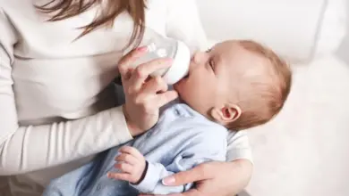 Matka krmití dítě kojeneckou láhví v útulném prostředí.