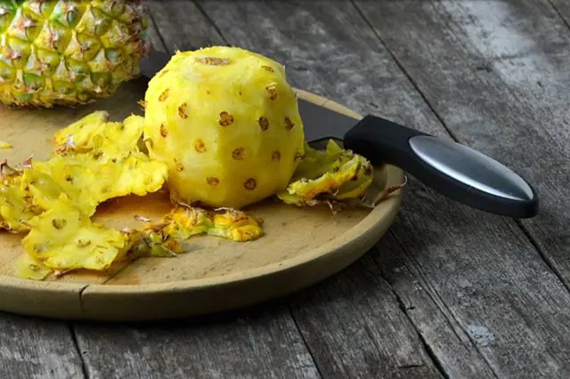Odlupovaný žlutý ananas na dřevěném prknu s nožem.