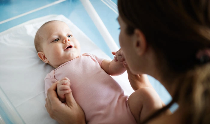 Matka drží ruce svému čtyřměsíčnímu miminku v nemocničním lůžku