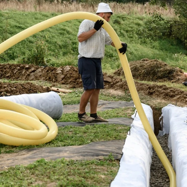 Muž instaluje žluté drenážní trubice pro odvodnění kolem domu.