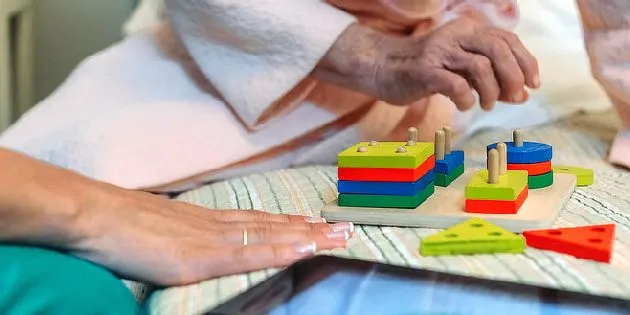 Starší ruce hrají s dřevěnými bloky při rehabilitaci pro parkinson.