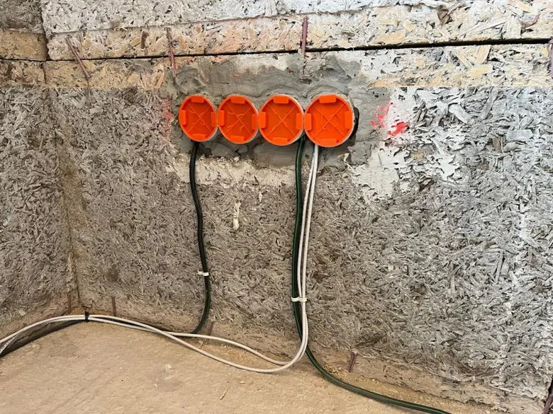 Čtyři oranžové elektrické krabice s vedením na stěně během plánování elektroinstalace.