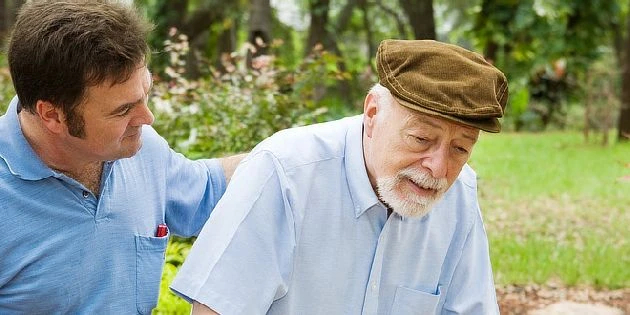 Mladý muž pomáhá starému muži s Parkinsonovou nemocí venku.