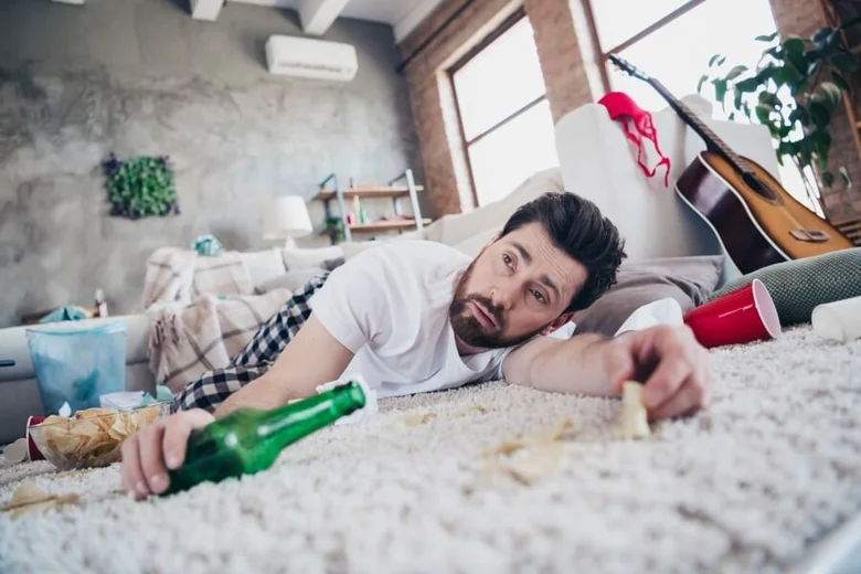 Muž leží na podlaze s lahví piva po pití alkoholu.