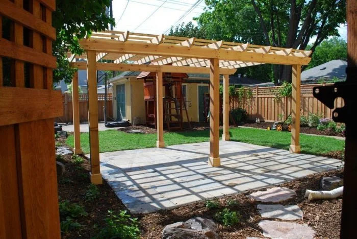Nově postavená dřevěná pergola na kamenné terase v zahradě.