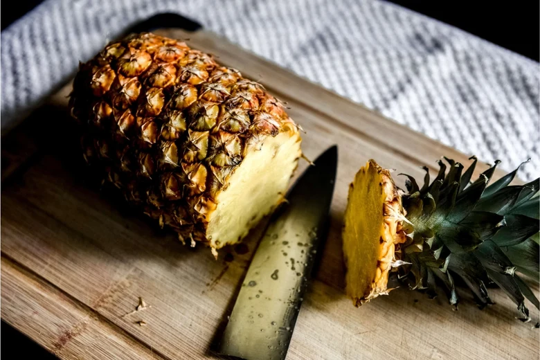 Ananas na dřevěném prknu po naporcování s nožem.