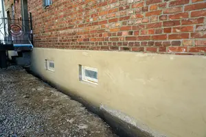 Vápenná omítka na spodní části cihlové zdi budovy.