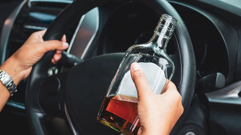 Ruce držící láhev alkoholu za volantem auta.
