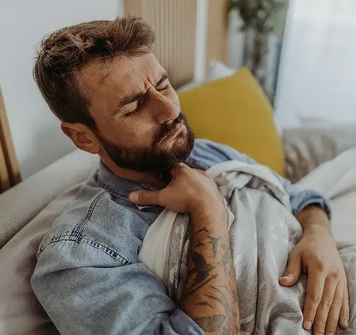Muž leží v posteli s příznaky chřipky jako je bolest hrdla.