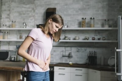 Žena v kuchyni drží břicho kvůli bolesti.